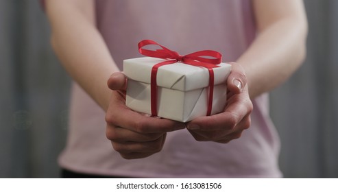 young woman stand and show white gift box with red ribbon bow
