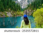 Young woman standing against a picturesque mountain landscape. Lake Kaindy is in the Kungey Alatau mountain range and is part of the northern Tien Shan. Kazakhstan, Kolsay Lakes National Park