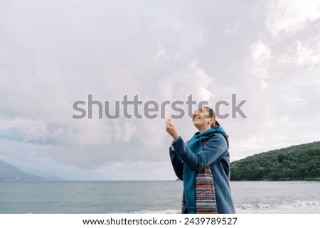 Young woman is standing by the sea with a kite spool in her hands, straightening the thread, and looking up