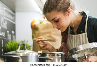 Young woman standing by the stove in the kitchen . - Shutterstock ID 1167501007