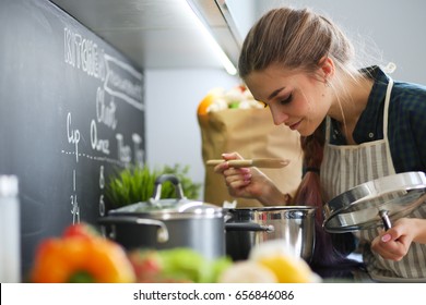 Young woman standing by the stove in the kitchen . - Shutterstock ID 656846086
