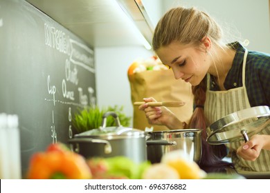 Young woman standing by the stove in the kitchen . - Shutterstock ID 696376882
