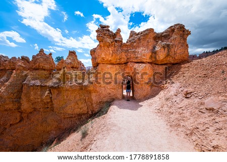 Young woman standing in desert landscape tunnel arch in Bryce Canyon National Park on Navajo loop Queen's Garden trail with sandstone rock formation