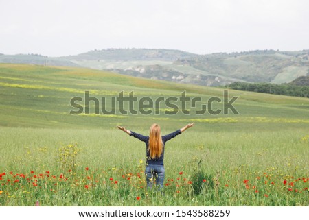 Young woman standing in the field of wild flowers with arms stretched out