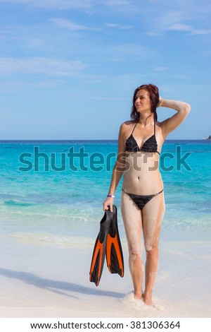 Young woman standing with flippers in front of blue warm sea