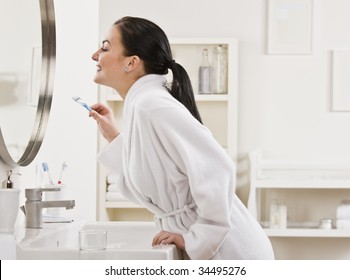 A Young Woman Is Standing In Front Of The Bathroom Mirror And Brushing Her Teeth.  Horizontally Framed Shot.