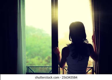 young woman standing in front of the bedroom window looking outside