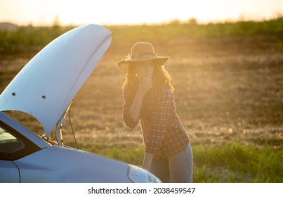 Young Woman Standing In Front Of Car With Popped Hood Thinking. Attractive Gilr Stranded At Roadside Fixing Vehicle.