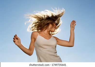 Young woman standing in front of sun tossing hair low angle view - Powered by Shutterstock