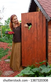 Young Woman Is Standing With A Fruit Bowl At Her Garden Shed