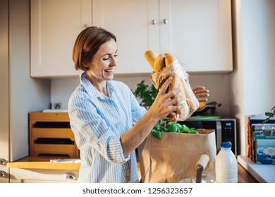 A young woman standing indoors in kitchen, unpacking shopping bag. - Powered by Shutterstock