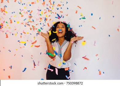 Young woman standing indoors under colorful confetti - Shutterstock ID 750398872