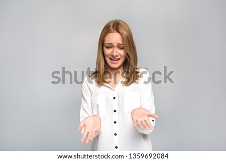 Young woman standing isolated on grey wall looking at hands confused unhappy