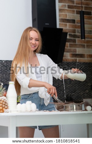 Young woman standing in the kitchen at home and cooking with enjoyment bakery products of flour, milk, cocoa, sugar and eggs. Funny portrait of happy girl chef 