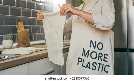 Young Woman Standing In The Kitchen Putting Reusable Cotton Produce Bags Into The Shopper Bag With Inscription NO MORE PLASTIC. Zero Waste Concept.