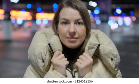 Young Woman Standing And Looking At Camera In Underground Parking Garage. Cars Parked In A Shopping Center Or Residential Building. Girl Driver In Jacket.