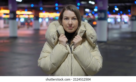 Young Woman Standing And Looking At Camera In Underground Parking Garage. Cars Parked In A Shopping Center Or Residential Building. Girl Driver In Jacket.