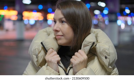 Young Woman Standing And Looking At Camera In Underground Parking Garage. Cars Parked In A Shopping Center Or Residential Building. Girl Driver In Jacket.