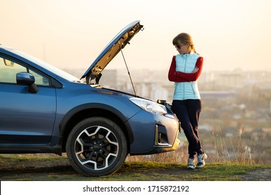 Young Woman Standing Near Broken Down Car With Popped Up Hood Having Trouble With Her Vehicle. Female Driver Waiting For Help Beside Malfunction Auto.