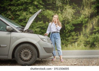 Young woman standing near broken down car with popped up hood having trouble with her vehicle. Waiting for help tow truck or technical support. A woman calls the service center.