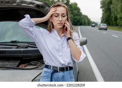 Young woman standing near broken down car with popped up hood having trouble with her vehicle. Waiting for help tow truck or technical support. A woman calls the service center. - Shutterstock ID 2201228209