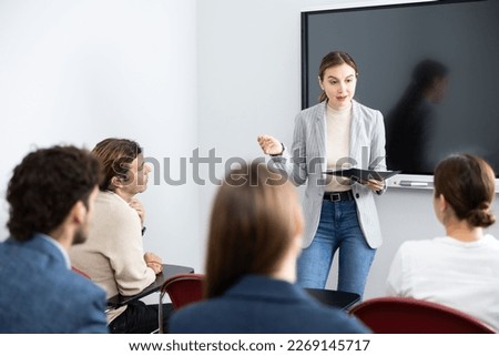 Young woman standing near interactive board and communicating with adult students during advanced training courses in classroom