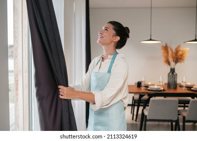 Young woman standing near the widnow and fixing the curtains
