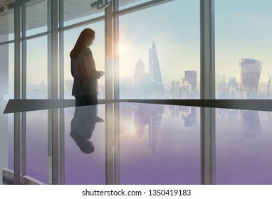 Young Woman Standing Next To The Office Window With Beautiful City Of London View And Reading Message On The Phone 