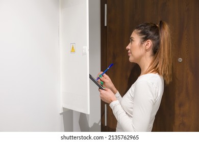 Young Woman Is Standing With Notebook And Writing Down The Electric Meter Reading