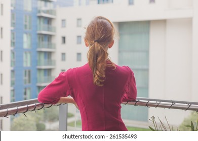 A Young Woman Is Standing On A Balcony Of An Apartment Building