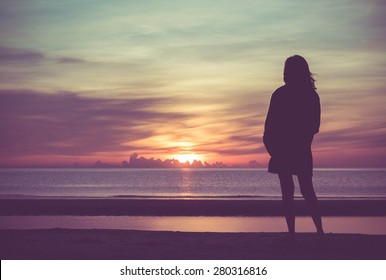 Young woman standing on the beach in sea and looking to sunrise.