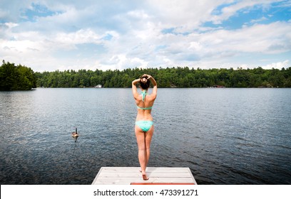 Young Woman Standing On A Dock With Geese On A Lake.