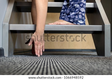 Young woman standing on the first step of the ladder bend down to reach the floor with fingers. Morning stretching exercise 