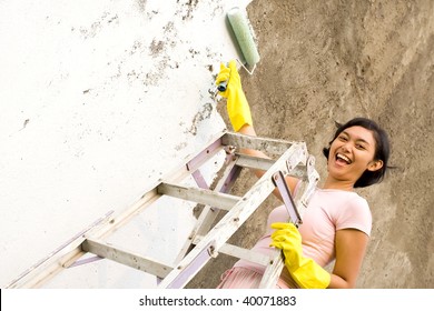 Young Woman Standing On A Ladder, Painting Exterior Wall Of Her House