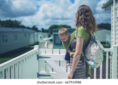 A Young Woman Is Standing Outside A Caravan In A Trailer Park With Her Baby In A Wrap