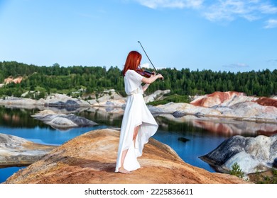 young woman standing in phacelia field. girl playing musical instrument called violin . concert in nature. violet flowers. lady wearing short white dress.
