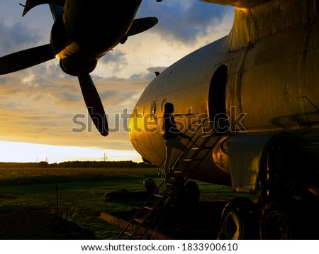 Young woman standing at plane ladder going to board, outdoors, airport. Old Soviet military airplane, sunset time. Close up of a Abandoned Historic AircraftAN-12. Close up of propeller engine. 
