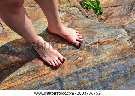 Young woman standing with red pedicured feet on a colored stone.