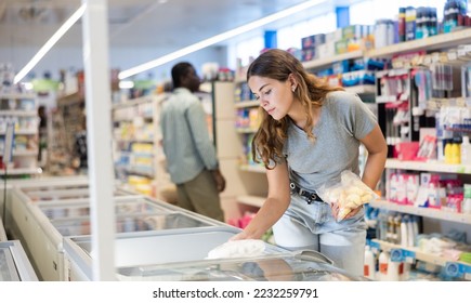 Young woman standing at refrigerator, choosing frozen convenience food in supermarket. - Shutterstock ID 2232259791