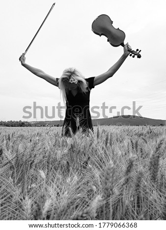 young woman standing in rye field and taking a bow with violin in hand