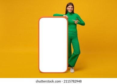 Young woman standing and showing with finger blank screen of huge phone, mockup for your app, isolated on yellow 