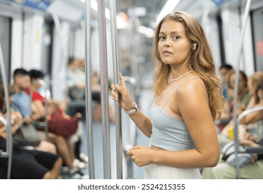 Young woman standing with smartphone and headphones riding in subway car - Powered by Shutterstock