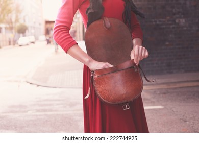 A Young Woman Is Standing In The Street With Her Handbag Open