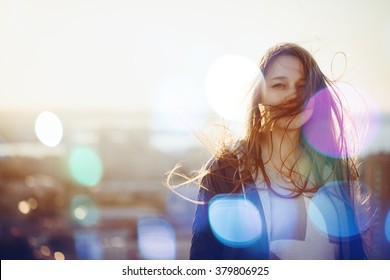 Young Woman Standing in Sunset Light, Looking at Camera. Hair Fluttering in the Wind. Selective Focus, Bokeh Lights. - Powered by Shutterstock