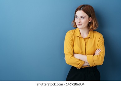 Young woman standing watching to the side with folded arms and a quiet smile over a blue background