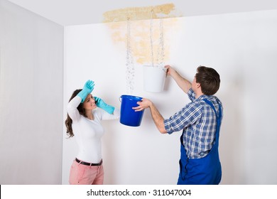 Young Woman Standing With Worker Collecting Water In Bucket From Ceiling In House