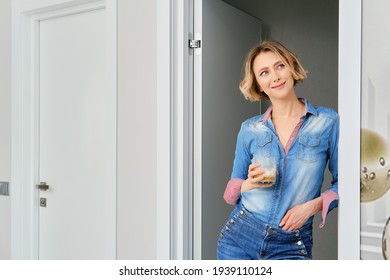 Young Woman Stands In The Doorway Of The Bedroom With A Glass Of Cappuccino In Her Hand