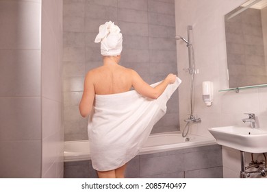 young woman stands with her back and takes off white towel to take a bath or shower. woman wipes herself off with a towel after shower
