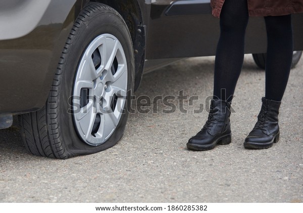 A young woman stands near her car with a flat tire,\
trouble on the road.