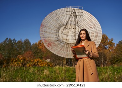 a young woman stands near a huge astronomical radar and holds documents in her hands. science, scientists - Powered by Shutterstock